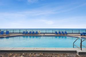 a swimming pool with chairs and the ocean in the background at AquaVista Beach Resort by Panhandle Getaways in Panama City Beach