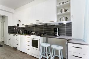 a white kitchen with white cabinets and stools at Forenom Serviced Apartments Helsinki Lapinlahdenkatu in Helsinki