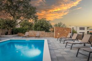 a swimming pool with lounge chairs and a sunset at Apartments Cesare with Shared Pool in Ližnjan