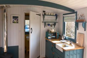 cocina con armarios azules, fregadero y ventana en Oak Shepherds Hut en Wootton Fitzpaine