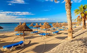 een strand met rieten parasols en stoelen en de oceaan bij Stunning Apartment - Near Los Cristianos in Chayofa