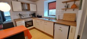 une petite cuisine avec des armoires blanches et une table orange dans l'établissement Zur alten Schmiede - Breitenbrunn/Erzgebirge, à Breitenbrunn/Erzgeb.