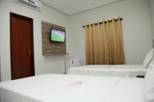 a room with two beds and a tv on the wall at Hotel Vale da Serra in Parauapebas