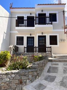 a white house with black windows and a stone wall at Achinos Apartments and Maisonettes in Kokkari