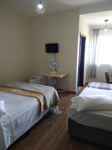 a room with two beds and a desk with a television at Hotel Pousada Icaraí in Poços de Caldas