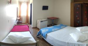 1 dormitorio con 2 camas, mesa y ventana en Hotel Pousada Icaraí, en Poços de Caldas