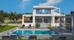 a villa with a swimming pool in front of a house at Johnny's White Luxury Villa in Tsilivi