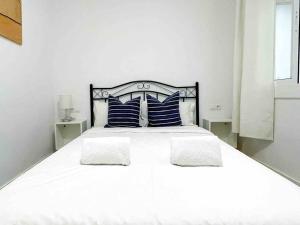 Una cama blanca con almohadas azules en un dormitorio blanco en @Hostourist Bcn Fira GranVia Plaza Europa-Justicia, en Hospitalet de Llobregat