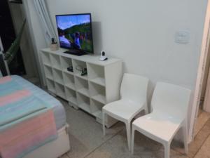 ein Wohnzimmer mit 2 weißen Stühlen und einem TV in der Unterkunft Apto frente ao mar, ar cond. frio e Wi-Fi in São Vicente