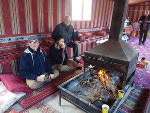 three people sitting on a couch next to a fireplace at Sun rise wadi rum camp in Wadi Rum