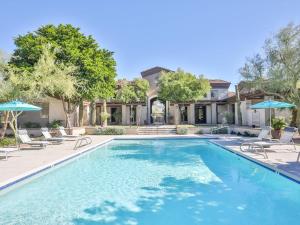 a swimming pool with chairs and umbrellas in front of a house at Pure Suites 2 Bed N Scottsdale McDowell Mtn Ranch Gym Pool in Scottsdale