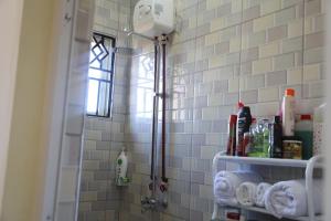 a shower in a bathroom with white tiles at Lovely Pearl Intercity Homes in Dar es Salaam