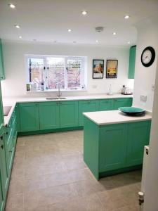 a kitchen with green cabinets and a clock on the wall at The Coach House- Stunning Detached Coastal home, with parking, by Historic Deal Castle in Deal