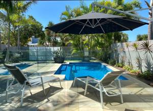 a pool with two chairs and an umbrella at The Palm - Beachside Home with Heated Pool & Cinema in Mudjimba