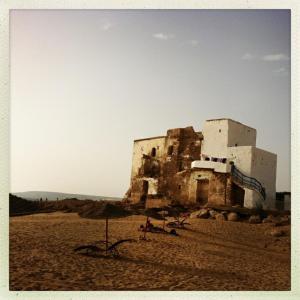 un vecchio edificio sulla spiaggia con persone sedute sotto un ombrellone di Hippie Chic House a Sidi Kaouki