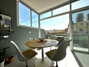 uma sala de jantar com mesa, cadeiras e janelas em Cosy Penthouse in Hamrun - Walking distance to Valletta em Hamrun