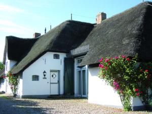 a white cottage with a thatched roof with pink flowers at FÖHRIENHAUS stilvolle 5 Sterne Einheiten in ruhiger Marschrandlage auf Föhr für Gäste, die das Besondere schätzen, gerne auch mit Hund in Midlum