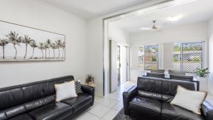 a black leather couch in a living room with palm trees at Sunnyvale 2 - Pet Friendly in Yamba