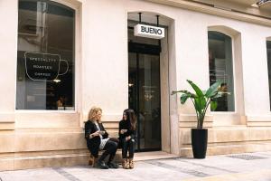two women sitting on a bench in front of a store at TOC Hostel Malaga in Málaga