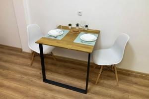 Una mesa de madera con dos sillas blancas y platos encima. en Cozy & fully equipped studio in the heart of downtown and next to Kalemegdan, en Belgrado