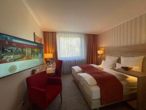 um quarto de hotel com uma cama grande e uma cadeira vermelha em Parkhotel Hohenfeld Münster em Münster