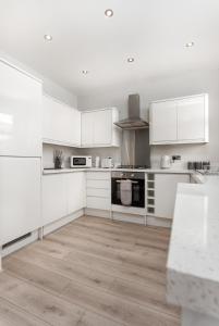a white kitchen with white cabinets and a wooden floor at Host Liverpool - Anfield Stadium Home, Cozy House for Family in Liverpool