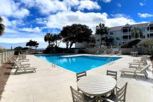 a swimming pool with chairs and a table and a building at Port O' Call E302 - Top Floor Ocean View Condo! in Isle of Palms