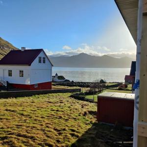 una casa bianca e rossa accanto a un corpo d'acqua di New flat with hot tub - No1 a Oyndarfjørður