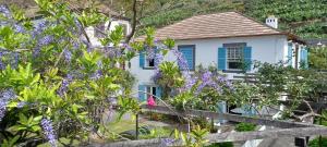 a white house with blue shutters and purple flowers at Casa da Madalena do Mar in Madalena do Mar