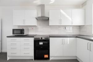 uma cozinha com armários brancos e um fogão preto em Roomy 3 bedroom house, 2 baths em Edgware