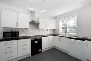 a kitchen with white cabinets and a black appliance at Roomy 3 bedroom house, 2 baths in Edgware +28 photos