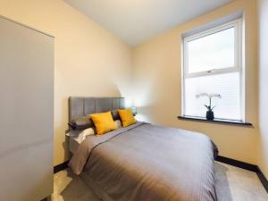 ein Schlafzimmer mit einem Bett mit gelben Kissen und einem Fenster in der Unterkunft Gibson Manor Apartment 10 in Wallasey