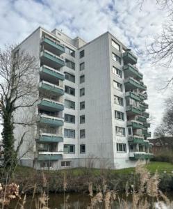 een hoog wit gebouw met groene balkons naast een rivier bij Up Wulkje21 Neu renovierte Wohnung mit PKW Stellplatz in Emden