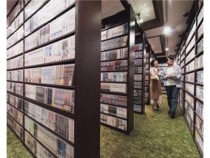 two people walking through a library aisle with books at Relief Kokura ANNEX Book & Stay in Kitakyushu