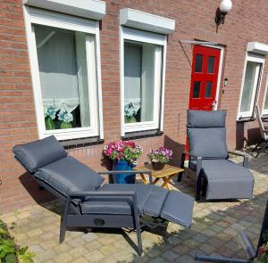 un patio con 2 sillas, una mesa y una puerta roja en B&B Poort van Westerwolde privé appartement met terras op zuiden, en Alteveer