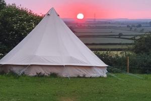 a white teepee in a field with the sunset in the background at French Tent secret garden glamping in Newark-on-Trent
