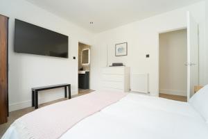 a white bedroom with a large bed with a flat screen tv at Beach Condos in Weston-super-Mare
