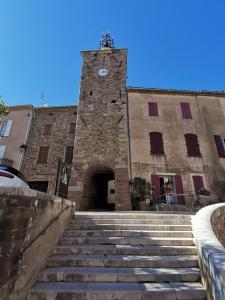 ein Steingebäude mit einem Uhrturm mit einer Treppe in der Unterkunft Appartement cozy au cœur du village in Roquebrune-sur-Argens