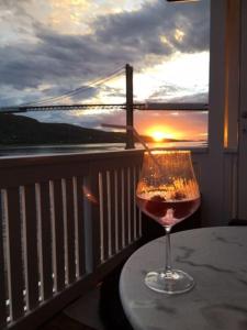 una copa de vino en una mesa en un balcón con vistas a la puesta de sol en Sjøhus ved Tjeldsundet - House by the sea en Evenskjer