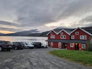 a large red building with cars parked next to a body of water at Sjøhus ved Tjeldsundet - House by the sea in Evenskjer