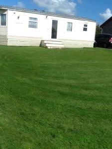 a white house with a green lawn in front of it at Rhosfeillion Static Caravan in Llangefni