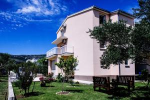 a white house with two benches in the yard at Apartman Sunny Vacay in Kaštela