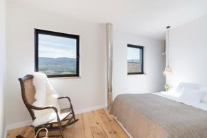 a bedroom with a bed and a chair and two windows at Casa da Zanjas in Seia