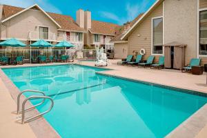 a swimming pool with chairs and umbrellas next to a house at Residence Inn Sacramento Cal Expo in Sacramento