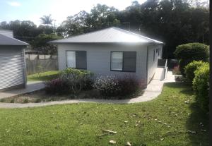 a small white house with a grass yard at Walk to Flynns , Nobbys Beach - Tranquility amongst the Rainforest in Port Macquarie