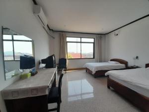a bedroom with two beds and a desk with a television at Mittaphap Hotel Oudomxai in Muang Xai