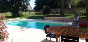 a pool with a wooden table and chairs next to a table and a tablektop at Le Clos des Roses in Chorey-lès-Beaune