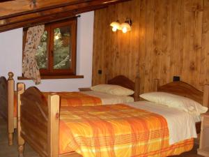two beds in a bedroom with wooden walls and a window at Residence Les Myosotis in Champoluc