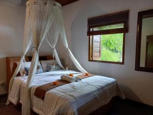 1 dormitorio con cama con dosel y ventana en Frangipani Inn & Restaurant, en Seraya