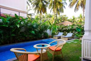 a patio with chairs and a table next to a pool at Elivaas Celest Luxe 4BHK Villa with Pvt Pool near Baga in Old Goa